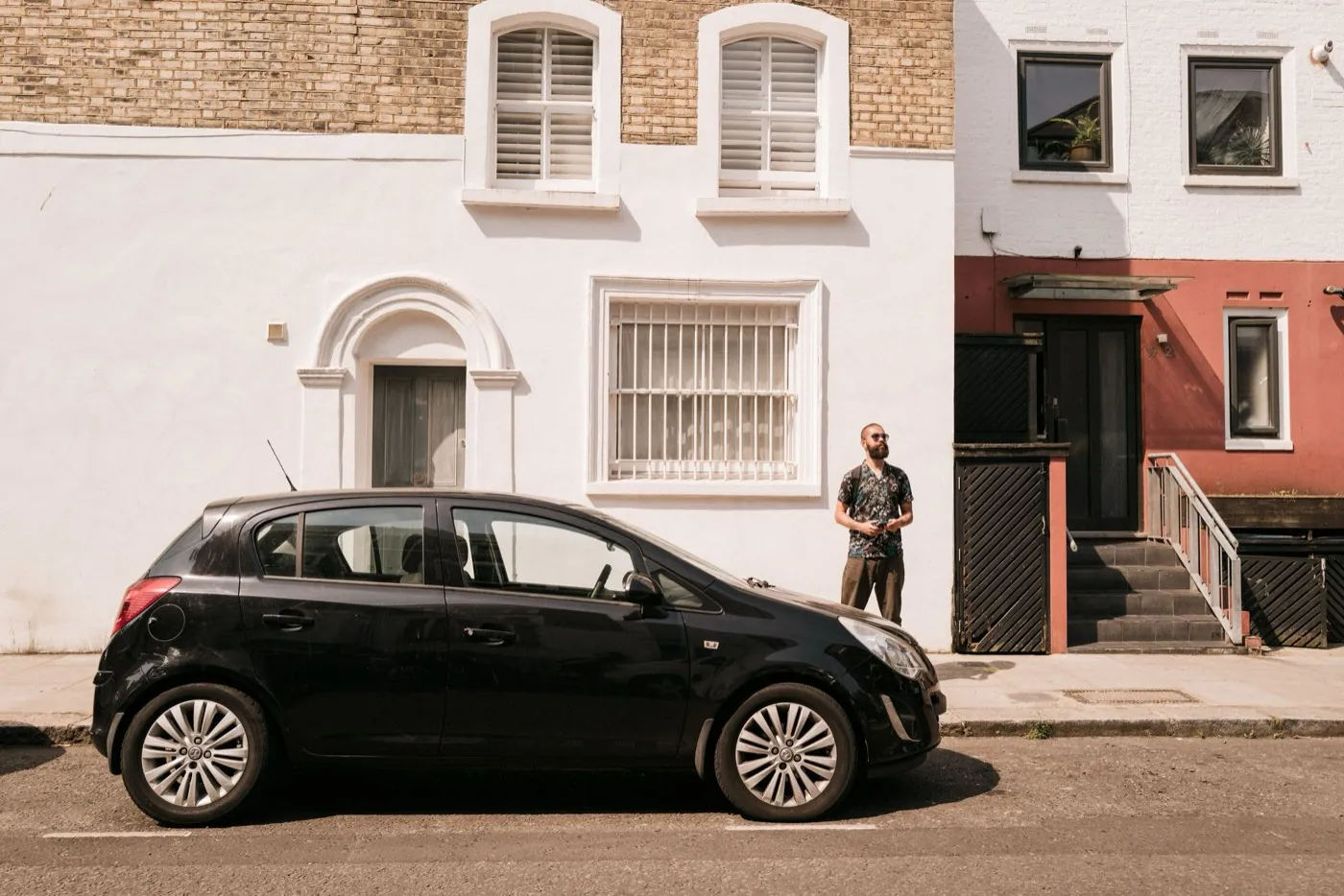 A man standing beside his black Vauxhall Corsa on a sunny London terraced street
