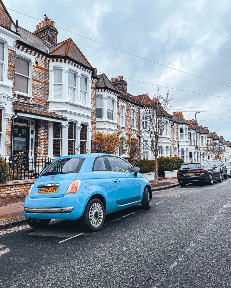 A sky-blue Fiat 500 parked on a terraced street in London