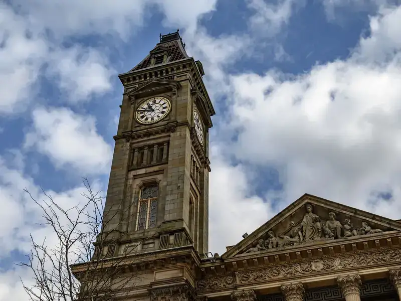 The clock tower and carved pediment of Bolton Town Hall against a blue sky with clouds
