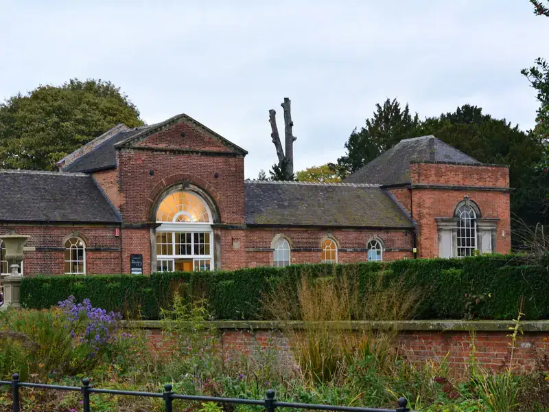 A Georgian red-brick garden building with an arched window, behind a hedge and flower border in a Derby park