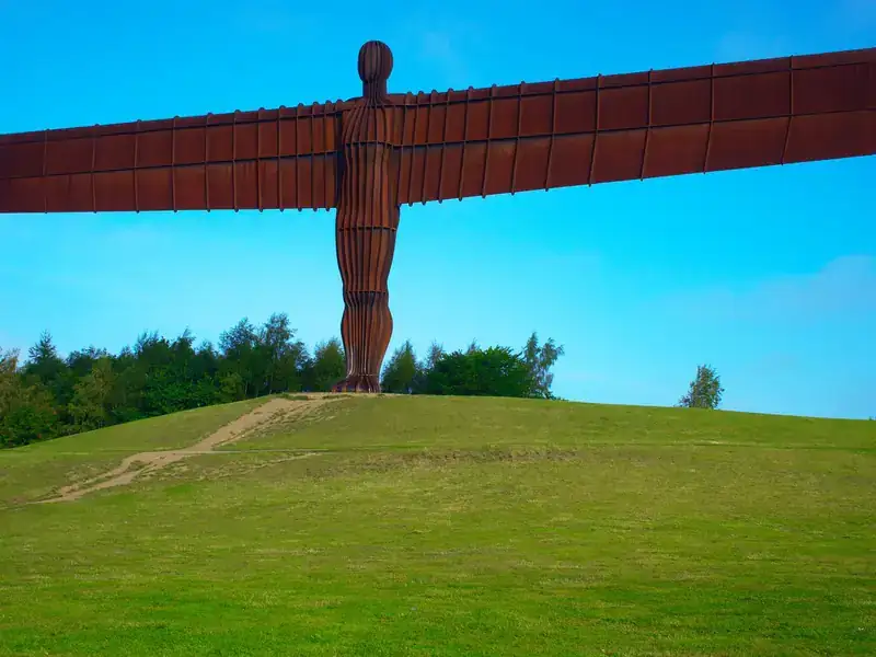 The Angel of the North sculpture on its grassy hill in Gateshead under a blue sky
