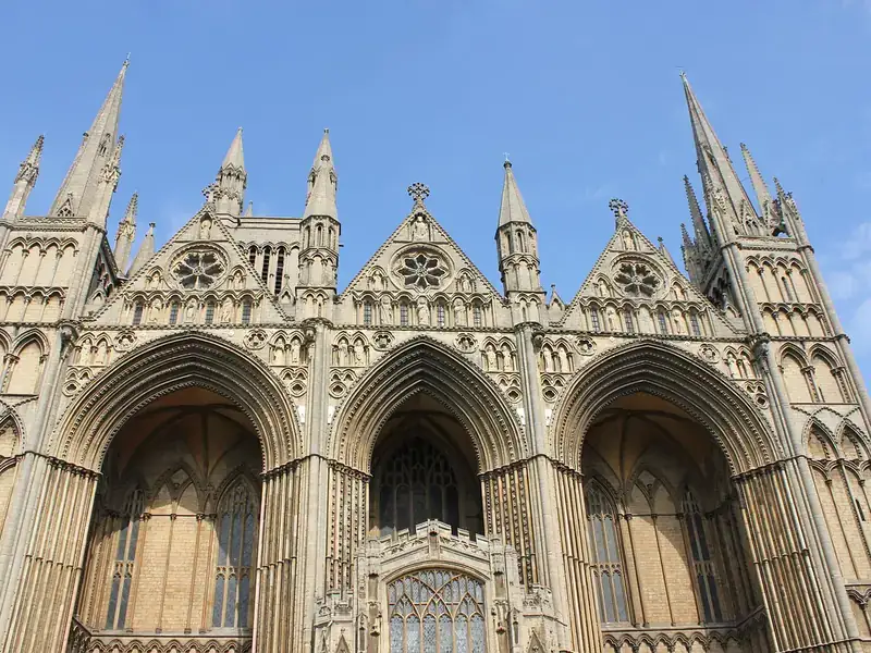 The west front of Peterborough Cathedral, with its three great arches, under a blue sky