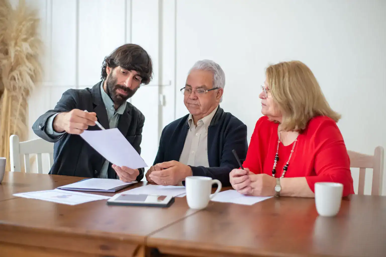 An adviser points to paperwork while talking an older couple through their options at a table