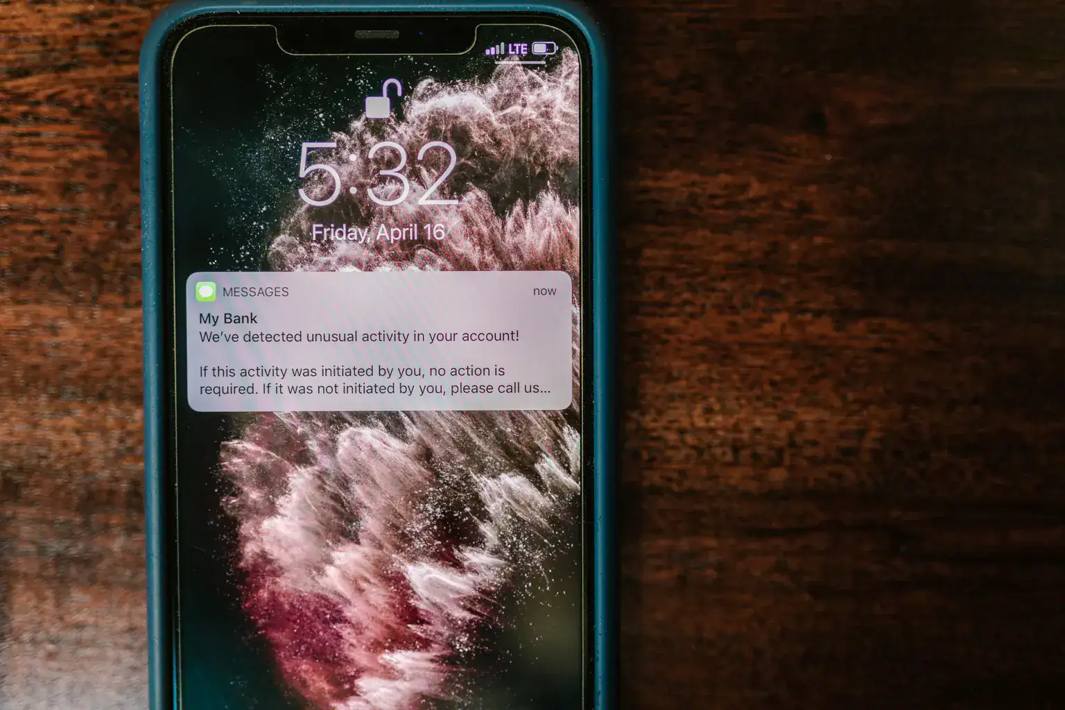 A phone lock screen showing a text message warning of unusual activity on a bank account