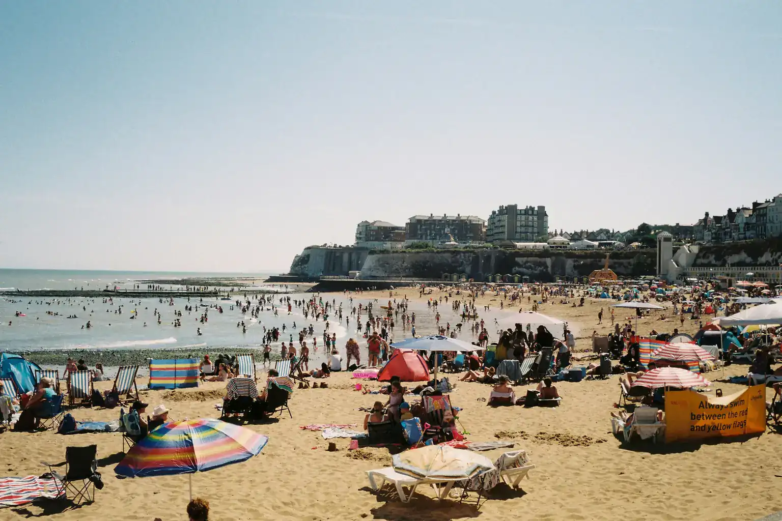 A packed sandy beach in Kent on a sunny summer day, with families, windbreaks and parasols