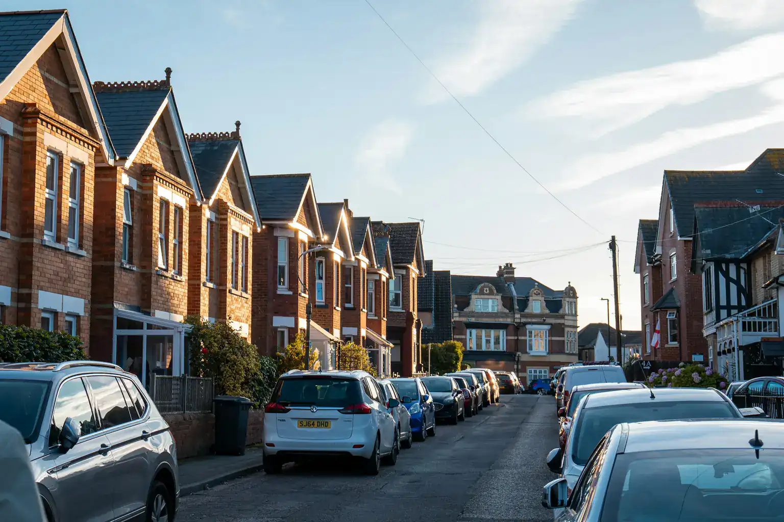 Cars parked along both sides of a British street of red-brick terraced houses