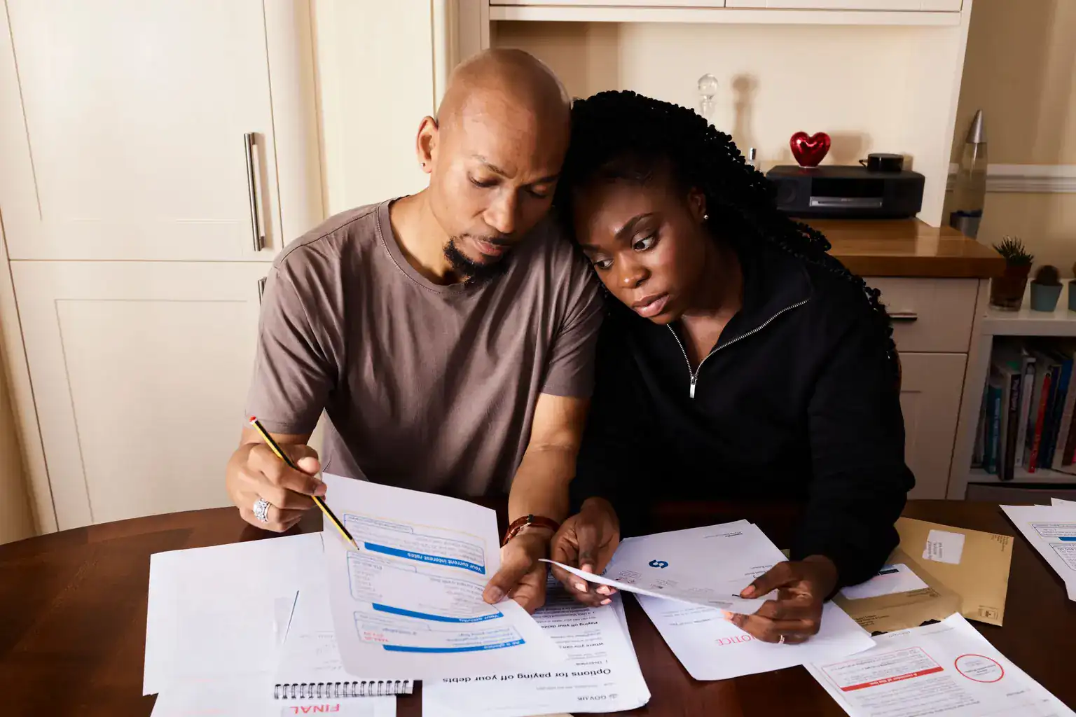 A couple sit close together at a dining table, checking household bills and paperwork