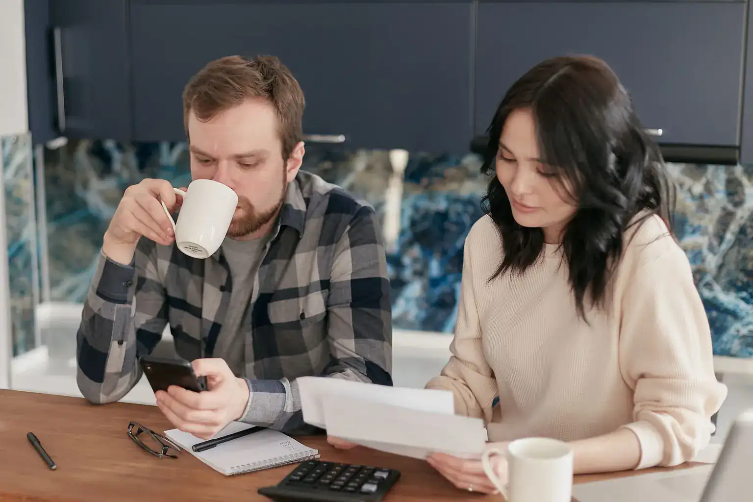 A couple at their kitchen table going through bills with a calculator and phone