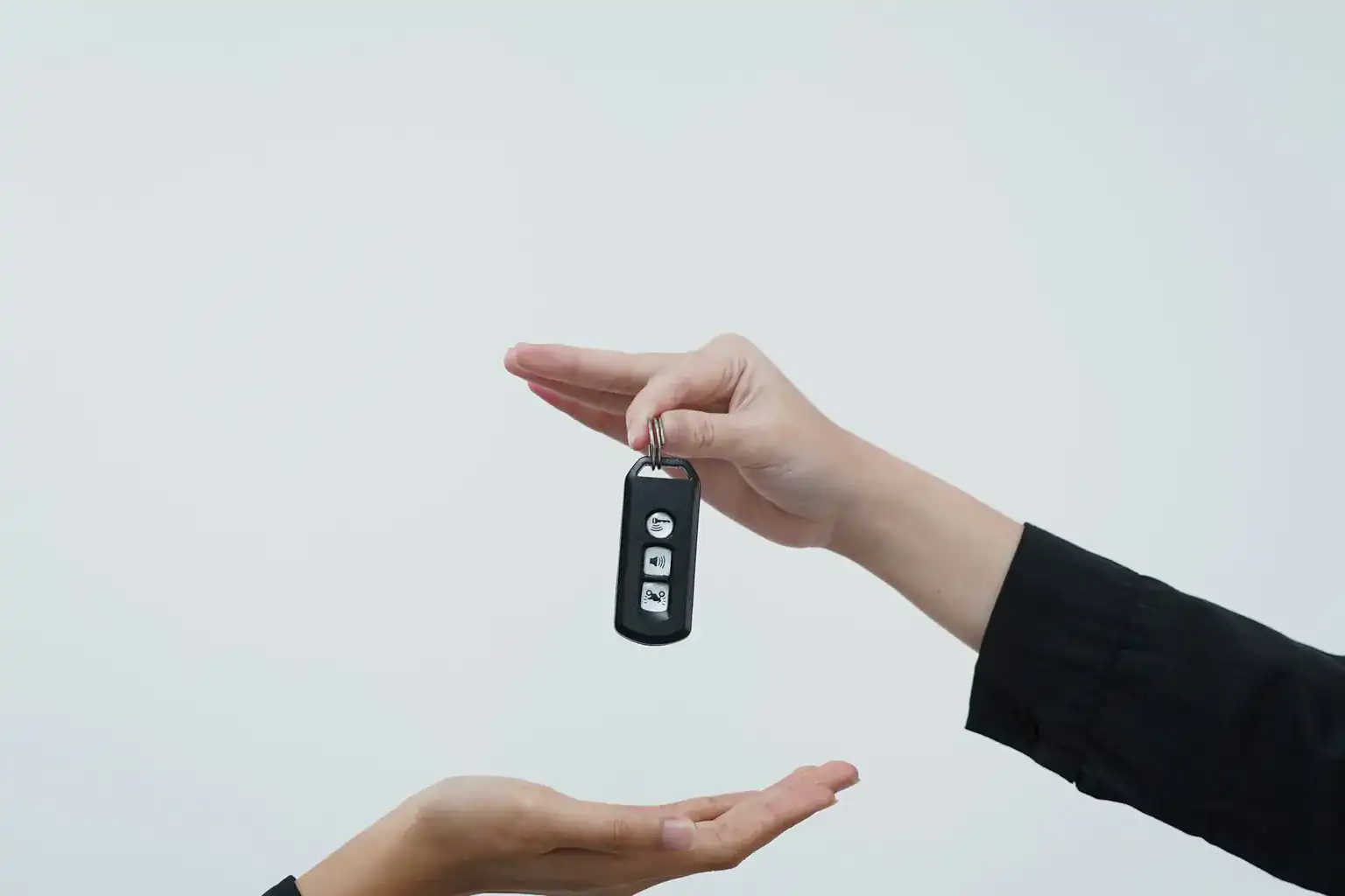 One hand dangles a car key fob above another person's open palm