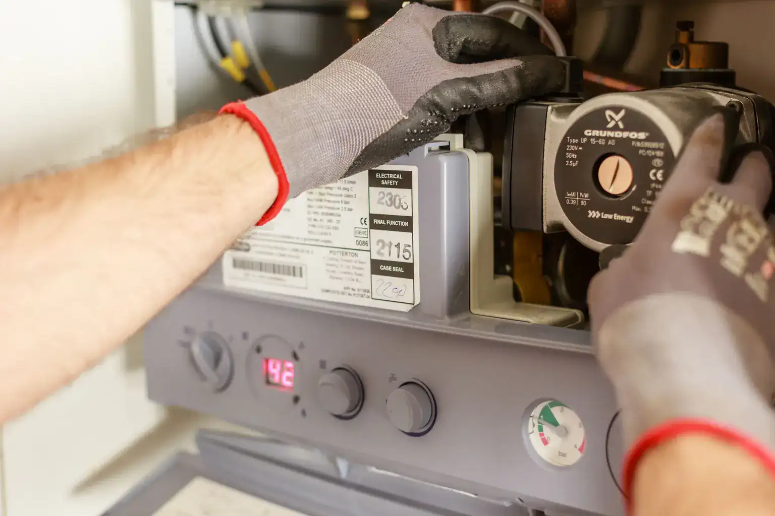 A heating engineer in work gloves repairing the pump inside an open gas boiler