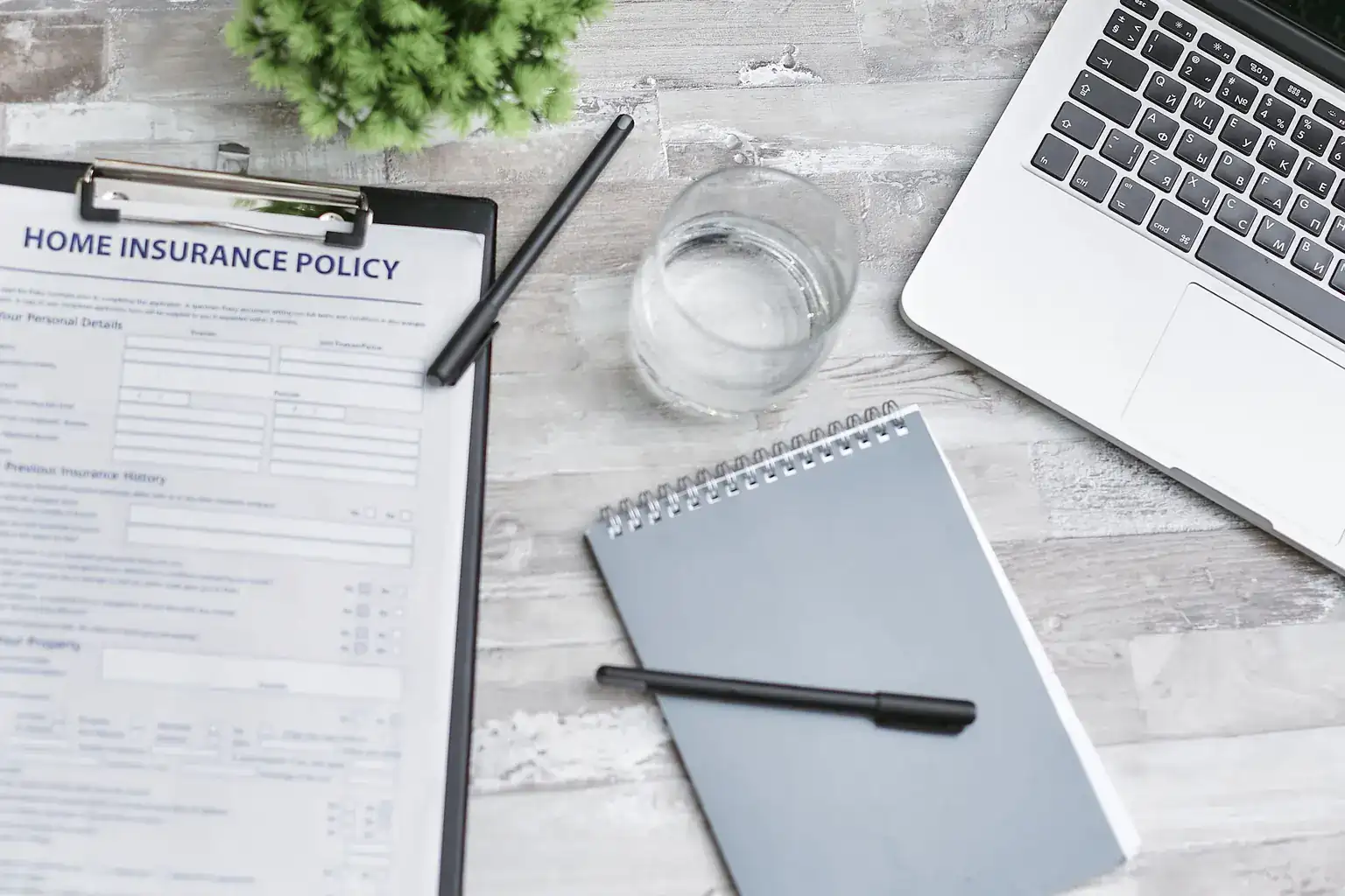 A home insurance policy form on a clipboard beside a notebook and laptop