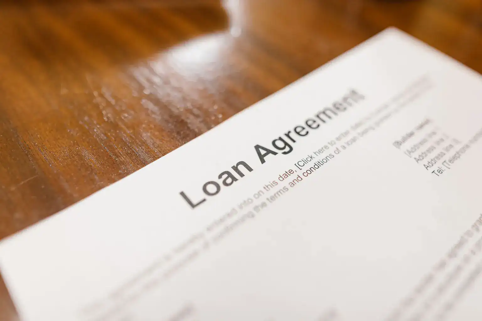 A printed loan agreement setting out the terms and conditions lies on a wooden table