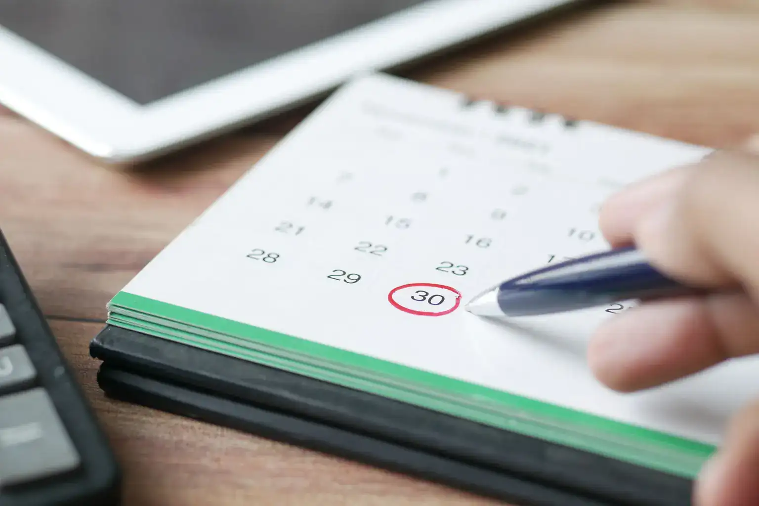 A hand circles a date on a desk calendar with a pen