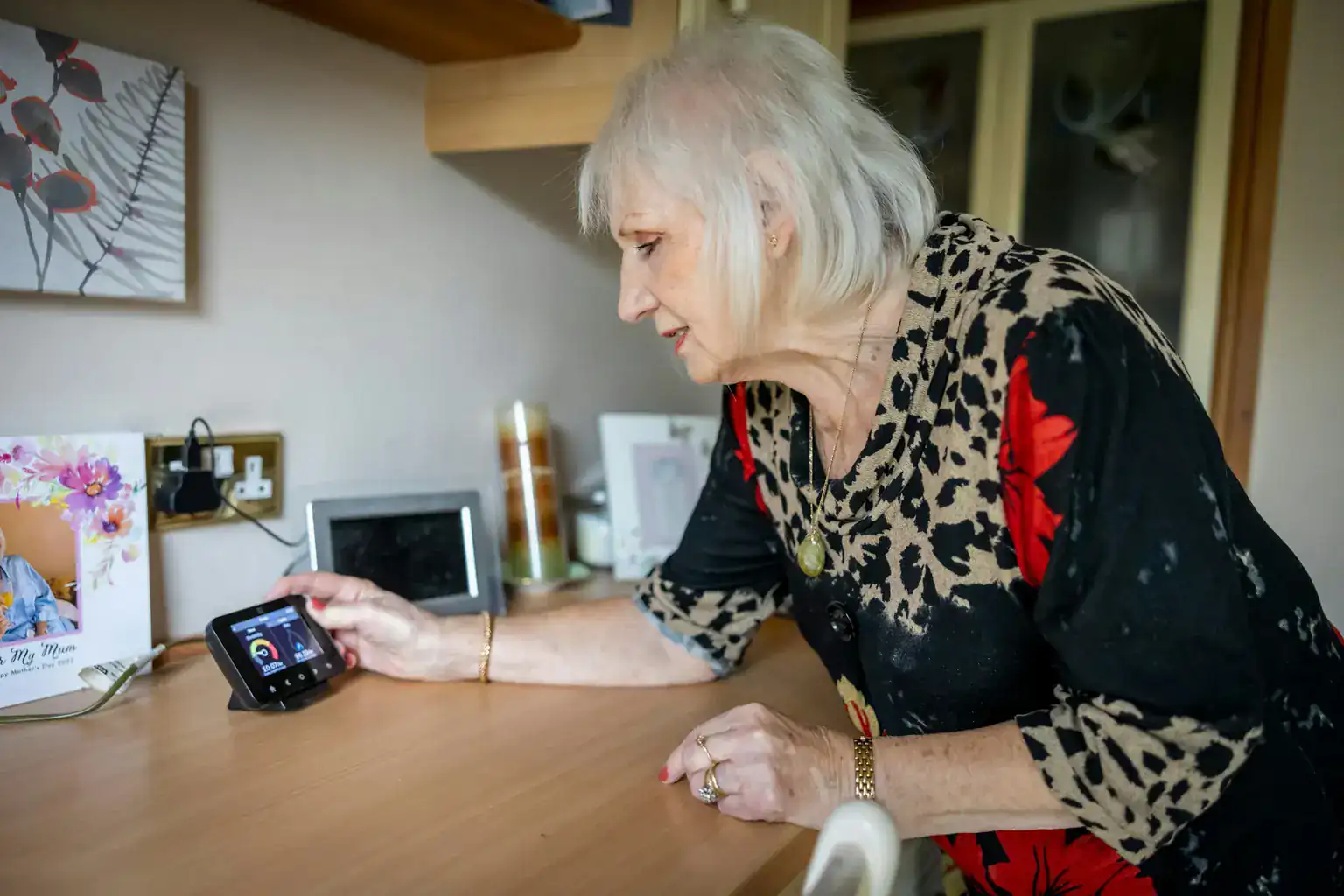 An older woman leans on her kitchen worktop to check a smart meter display