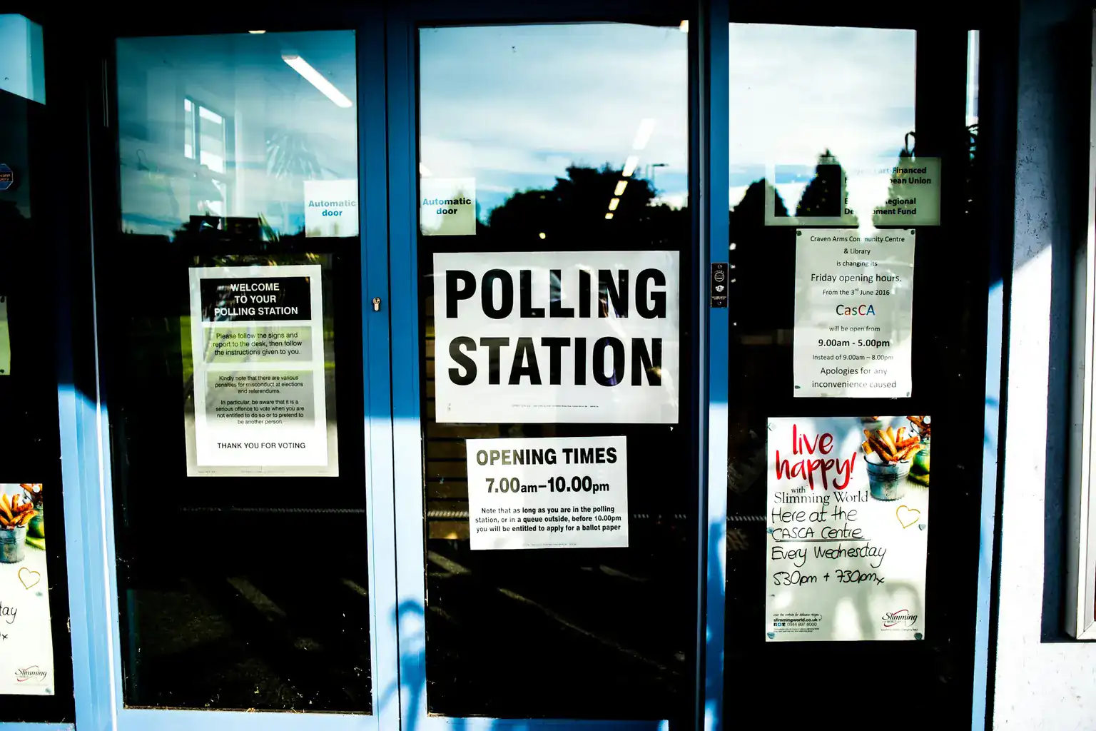Polling station and opening times signs on the glass doors of a community centre