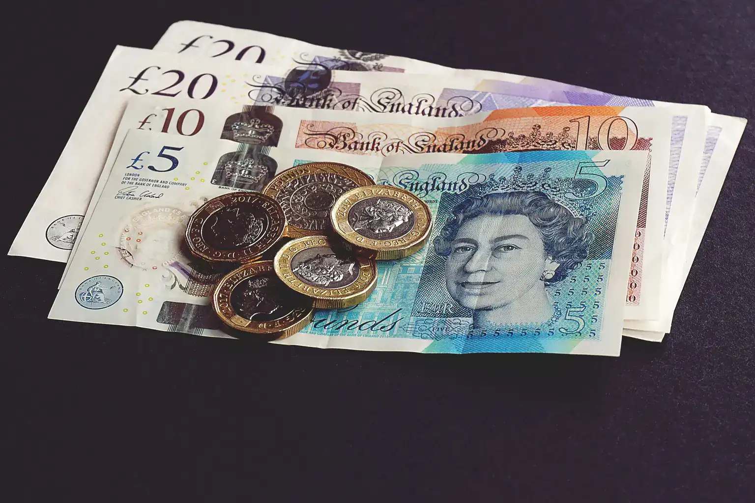 British twenty, ten and five pound notes with a few pound coins on a dark table