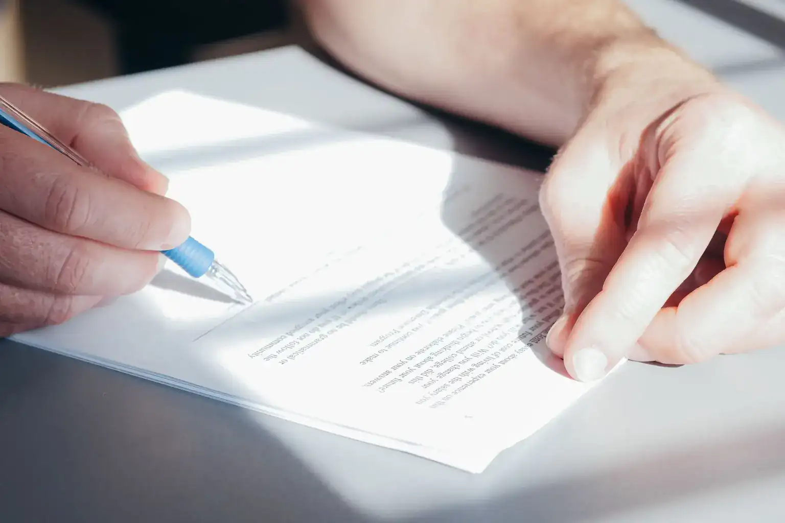 Close-up of hands signing a printed agreement with a blue ballpoint pen
