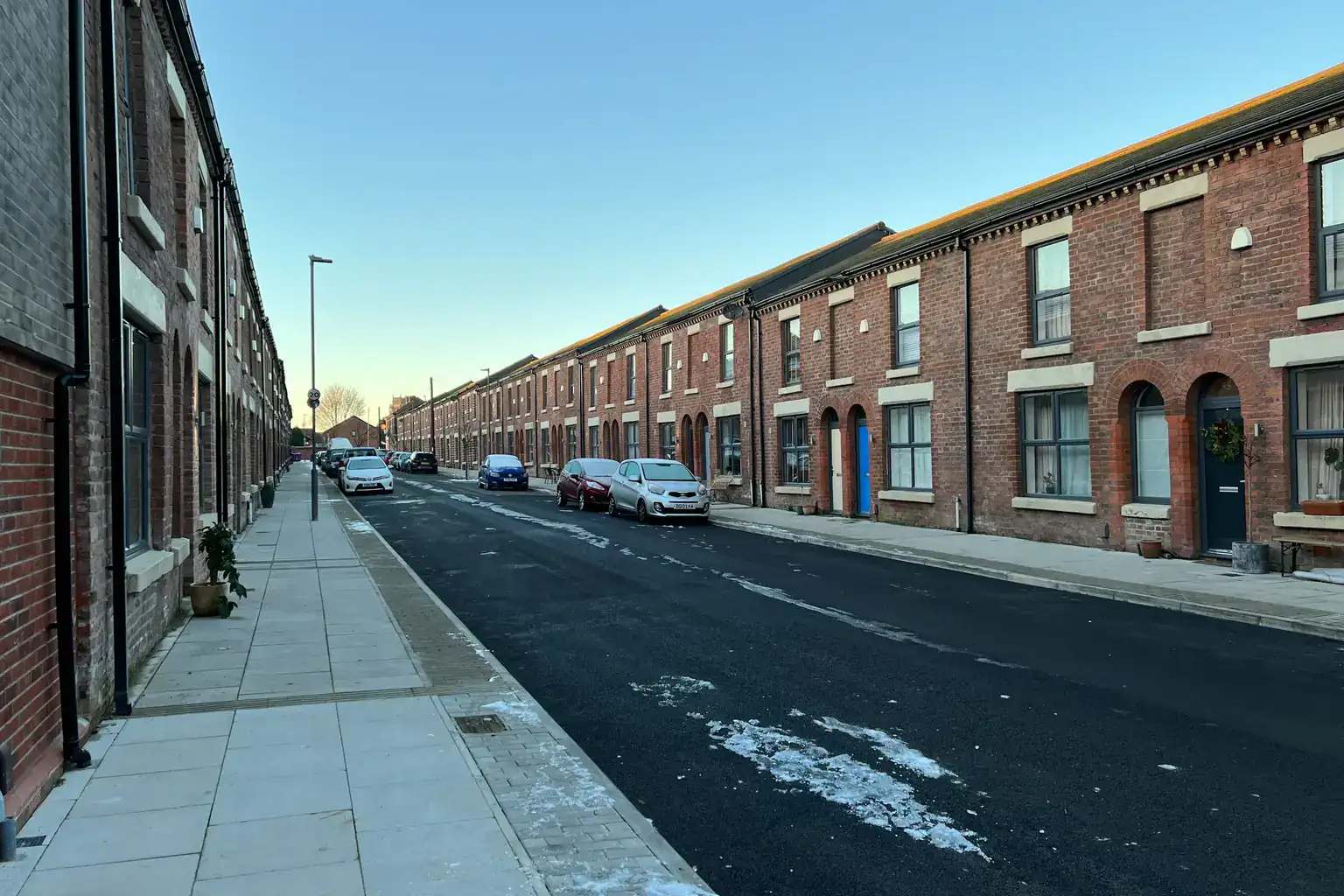 A long row of red-brick terraced houses lining a quiet residential street on a clear day