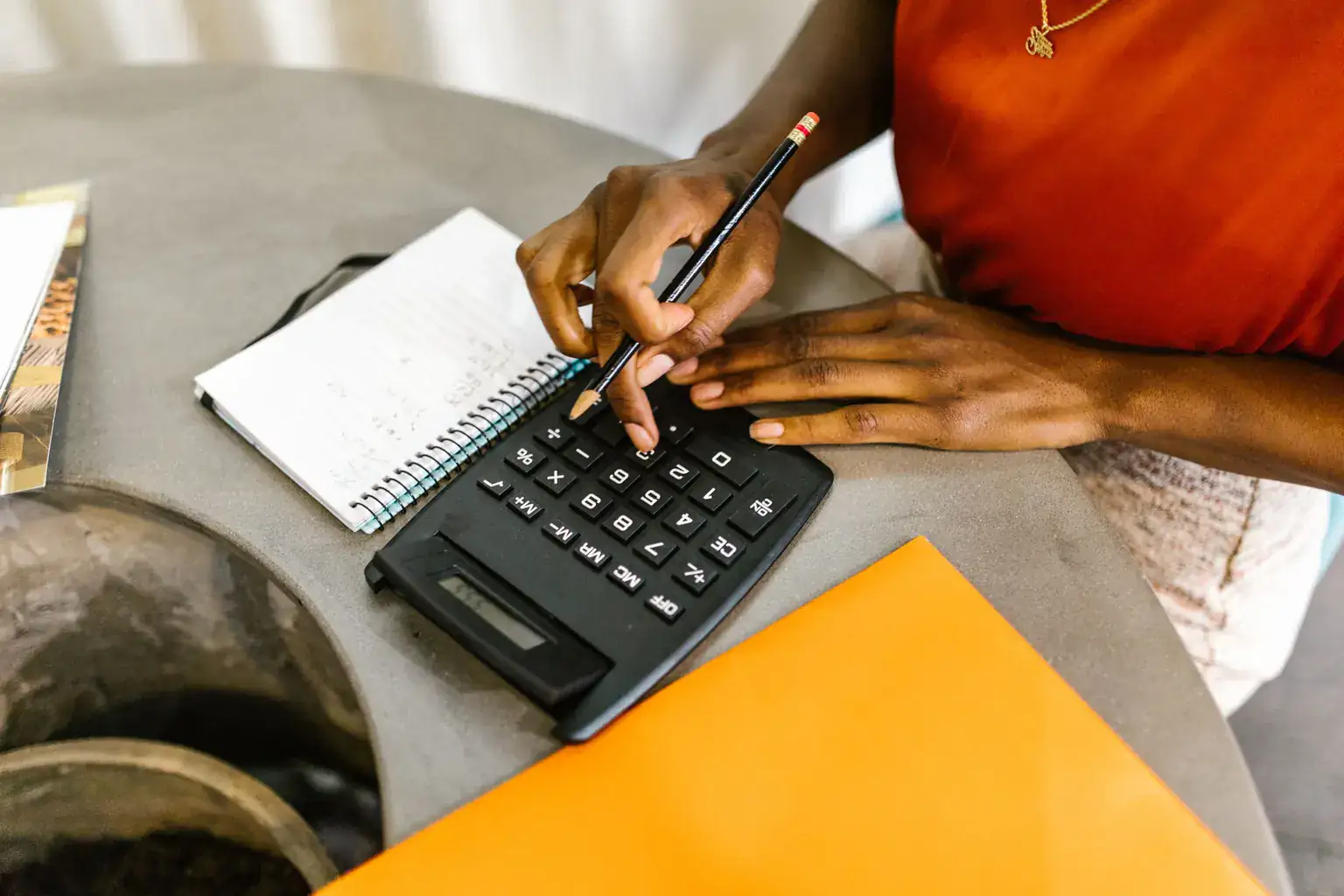 A woman works through her budget with a calculator, pencil and spiral notepad at a table