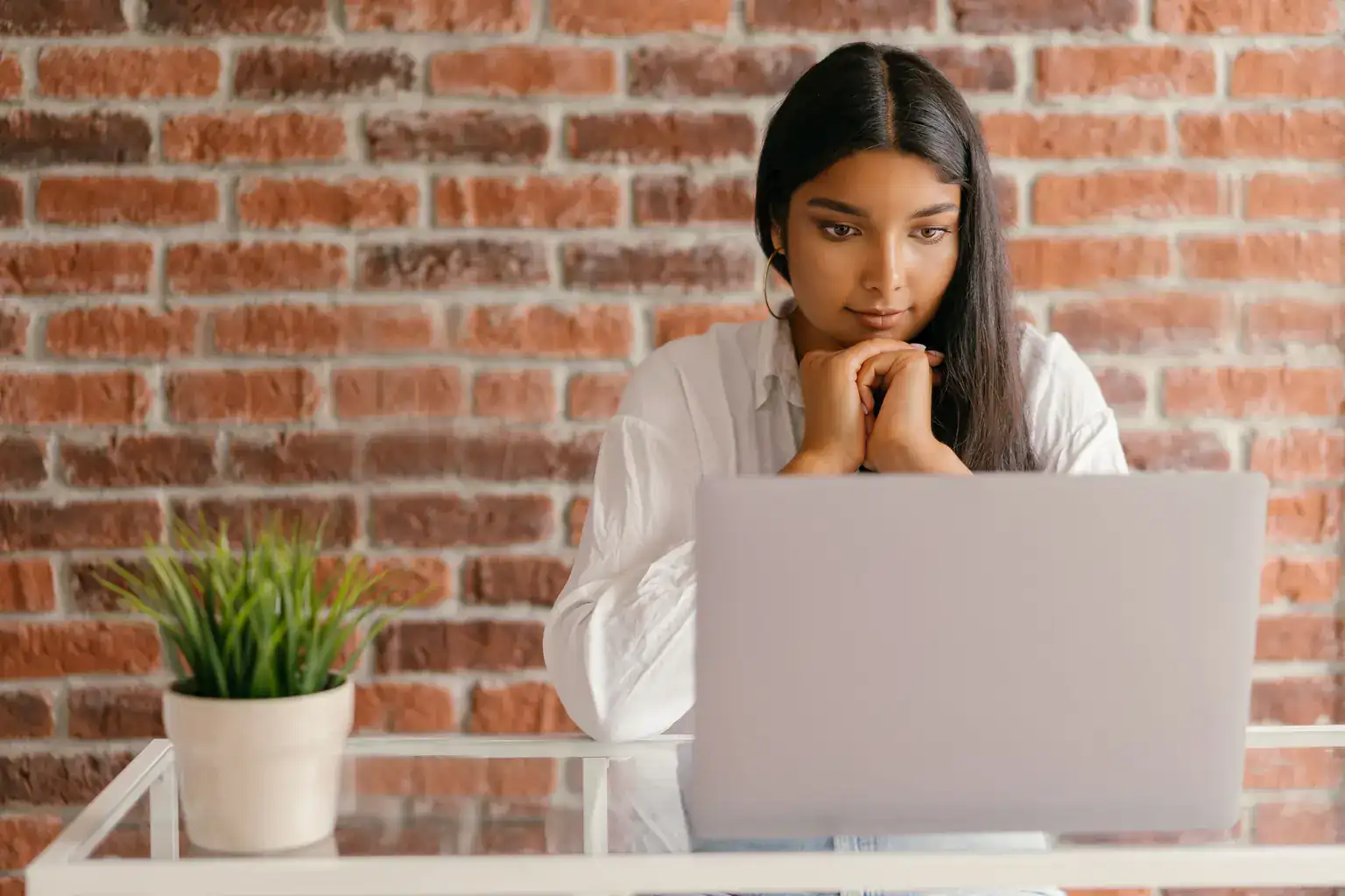 A young woman rests her chin on her hands while thinking over something on her laptop